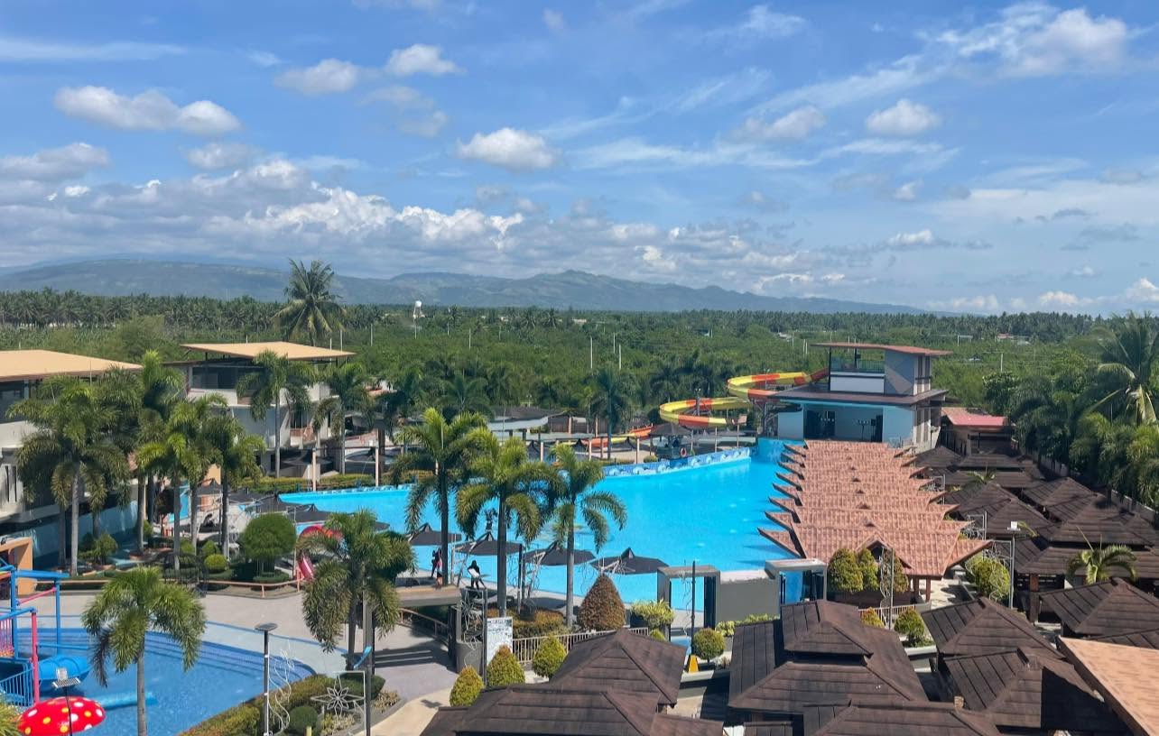 Wide landscape view across EmJake Aquawave Resort, its wave pool, water slides, cottages, palms, and surrounding hills