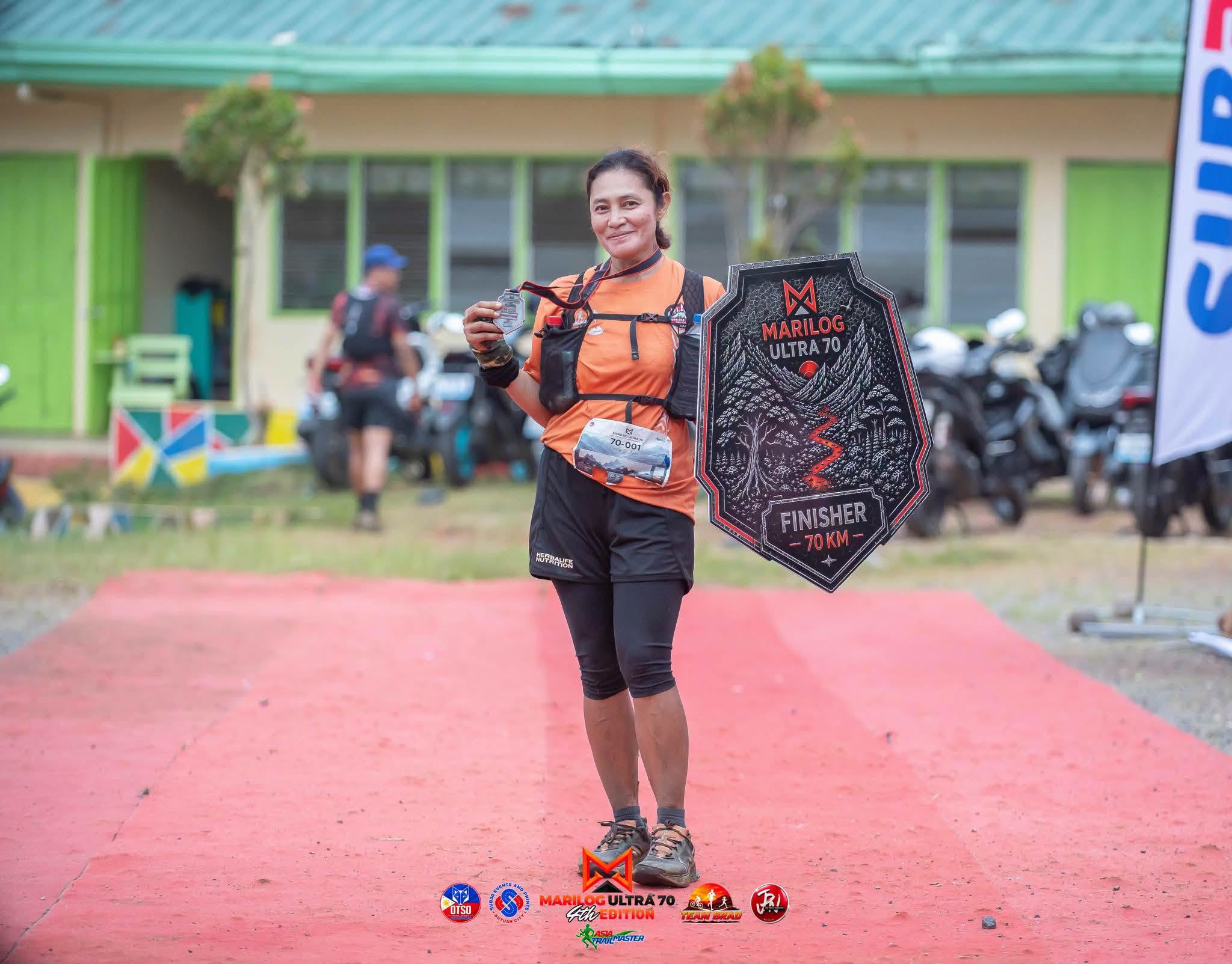 Irene Tan holding a medal and ultramarathon finisher award