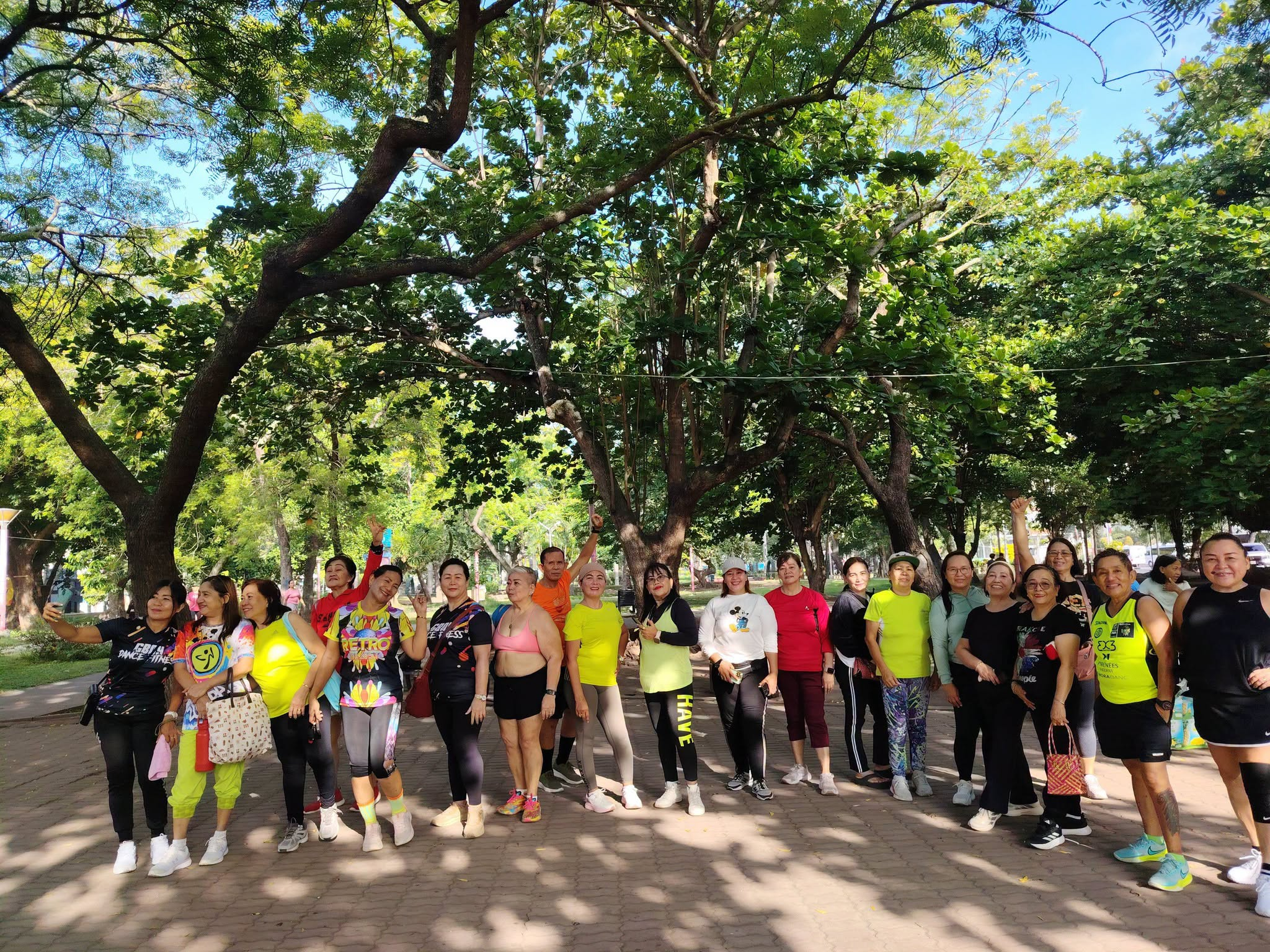 Group fitness participants posing under trees at Plaza Heneral Santos