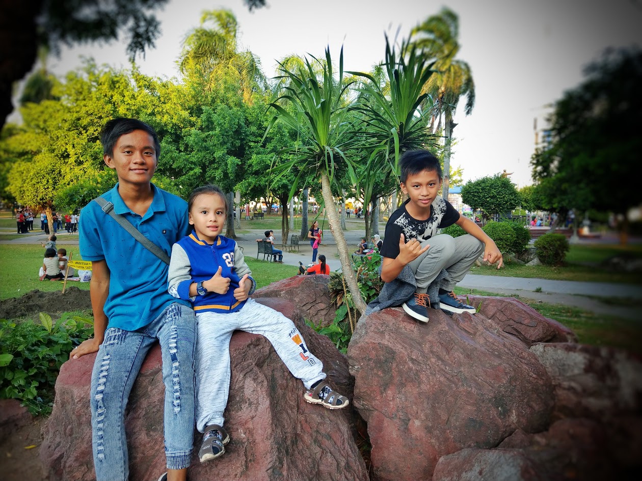 Visitors seated on decorative rocks inside Plaza Heneral Santos