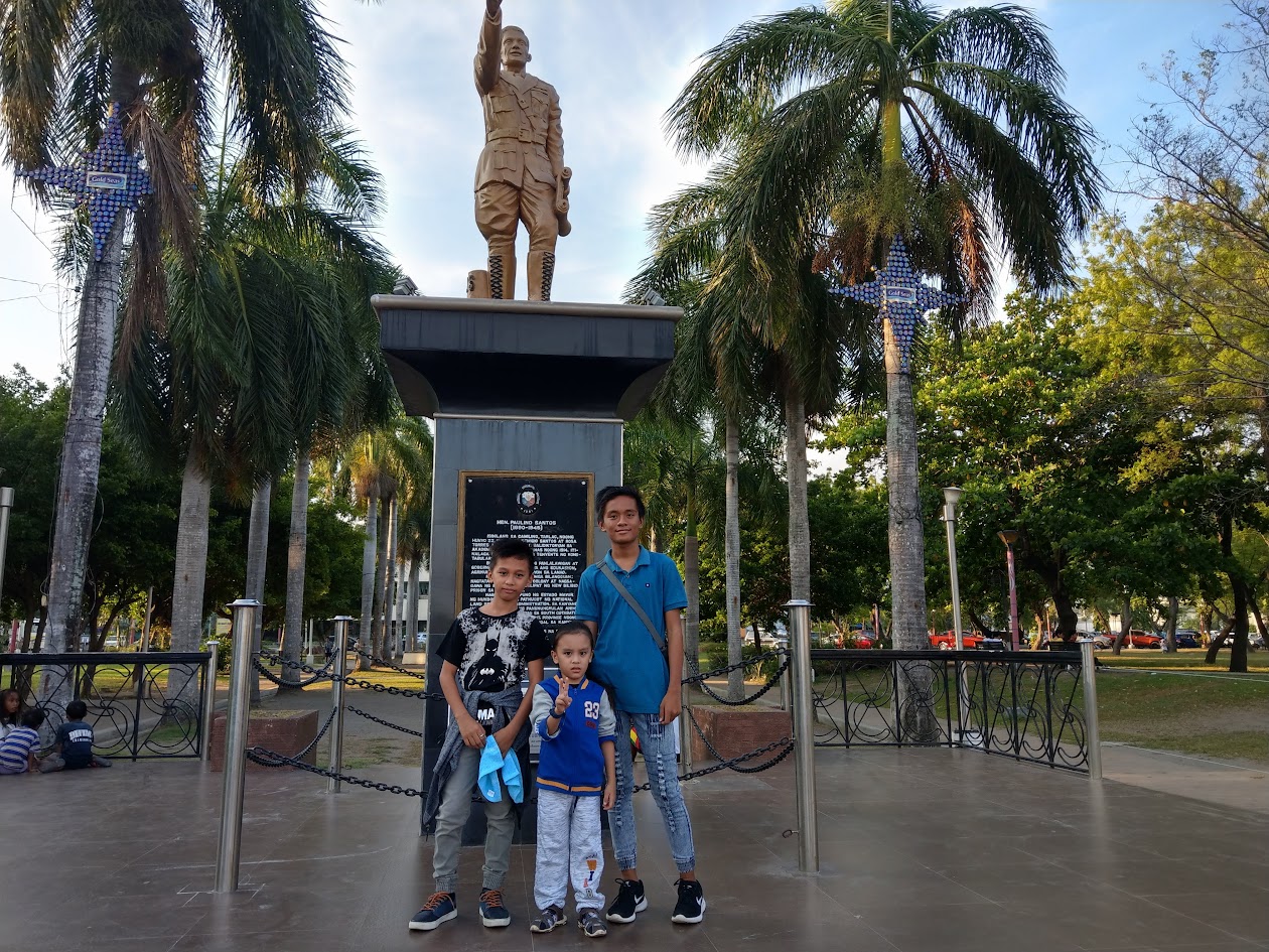 Visitors posing below the General Paulino Santos statue