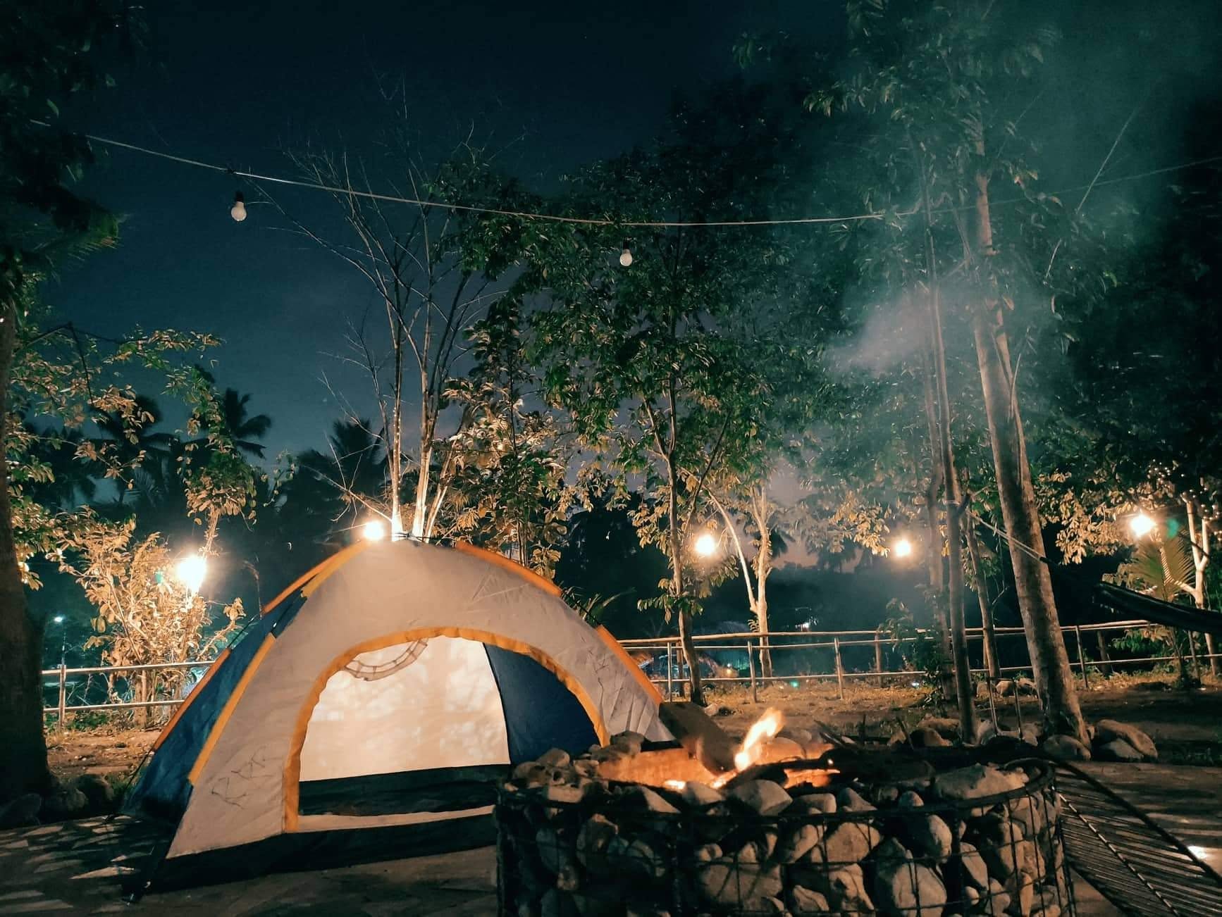 Tent beside a stone fire pit under the trees at night