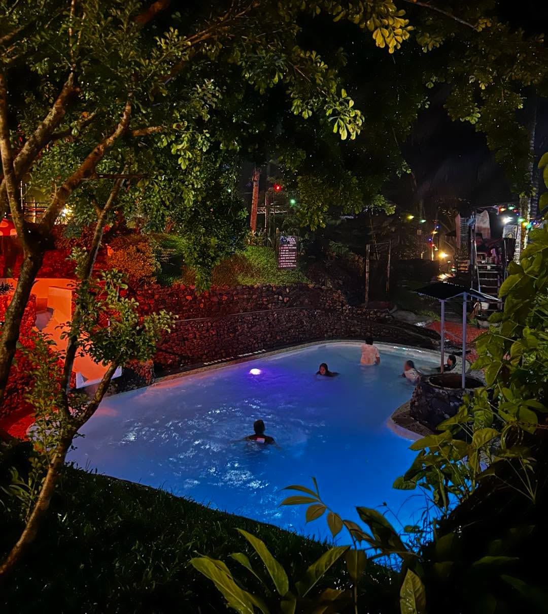 Visitors swimming in an illuminated pool at night