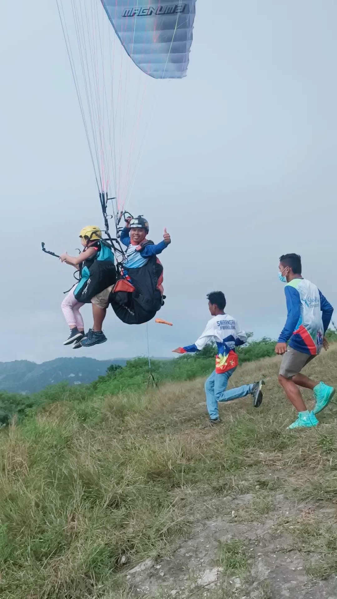 Tandem paraglider lifting from the launch field with ground crew nearby