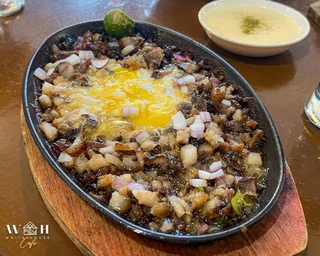 Sizzling platter with chopped browned meat, onions, egg, and dipping sauce